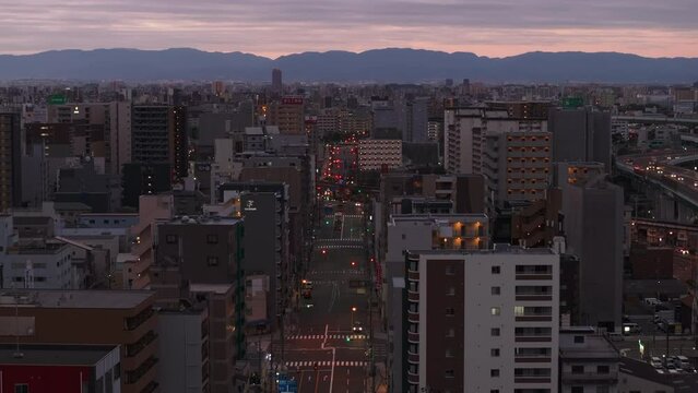 Aerial footage of streets and buildings in large city. Silhouette of mountain ridge against twilight sky in background. Osaka, Japan