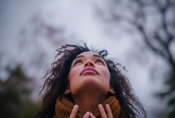 Upward angle of a woman gazing skyward, hands gently touching her neck, amidst a soft-focus backdrop, expressing contemplation and serenity.