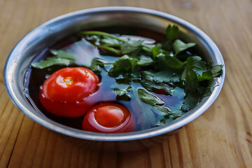 Fresh vegetables are being washed  in the metal bowl filled with cold water on the vintage cracked wooden cutting board. Organic tomatoes, parsley, celery. Side view. Selective focus. Bokeh