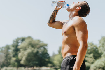 Caucasian athlete displays fit body and strong muscles during active outdoor training. Refreshing break for water, motivating and inspiring in natural environment.