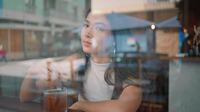Asian lady waiting cafe stirring drink by straw view from outside close up. 