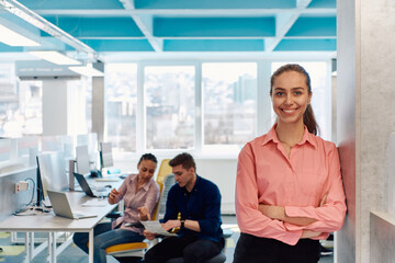 Portrait of young smiling business woman in creative open space coworking startup office. Successful businesswoman standing in office with copyspace. Coworkers working in background