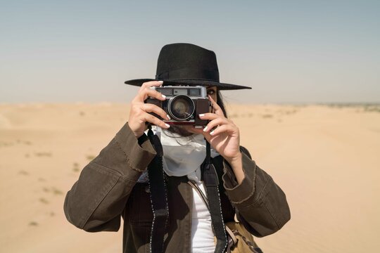 Arabic female traveler taking photos with film camera in the desert
