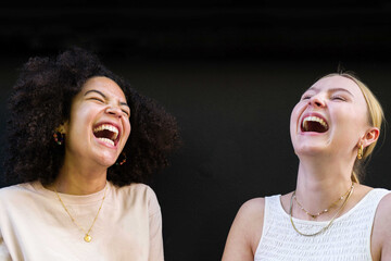Portrait of two young diverse female friends standing against black background talking