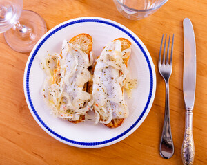 Slices of fresh wheat bread with crispy crust topped with pickled herring fillet and sliced marinated onions. Popular savory and tangy snack