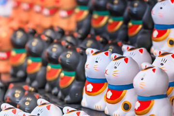 Obraz premium A bunch of aligned tiny and adorable stylized hand painted white Japanese manekineko cats lucky charm sculptures depicting to the famous beckoning cat and wearing bib adorned with a cherry blossom.