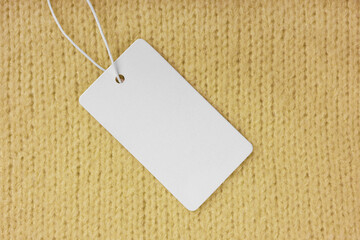 Blank clothing label on yellow knitted sweater background. Mockup, template with empty rectangular card, cloth tag for price or text. Shopping, sale, discount, black friday, fashion concept.