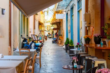 Papier Peint photo Lavable Ruelle étroite A narrow alley full of sidewalk cafes and shops in the historic old town of Aegina, Greece, on the island of Aegina, one of the Greek islands in the Saronic Gulf.