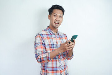 Adult Asian man holding his cell phone looking at camera with wow expression