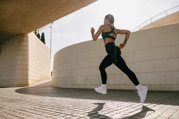 Foto op Aluminium Side view of woman athlete is jogging on morning on modern building background. Healthy life concept © Kostiantyn