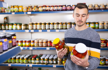 Adult man shopper in casual clothes chooses pickled cucumbers and tomatoes in store