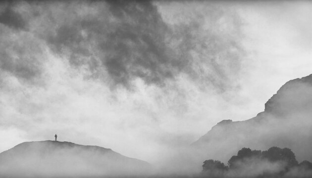 The forest and mountains behind very dense fog against a backdrop of clouds. A black-and-white landscape.