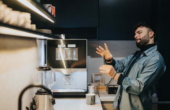 A 30 year old businessman in a light blue jacket impatiently checks his watch, waiting for his coffee in a modern kitchen.