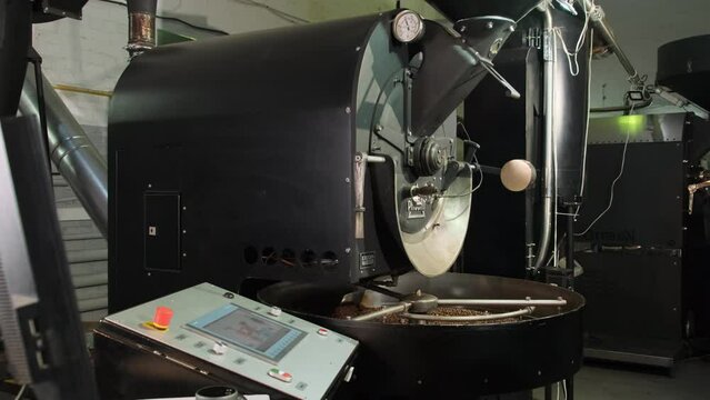 Roasting machine with cooling tray filled with hot coffee beans. Modern equipment with control panel for remote control in roastery