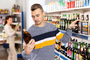 Adult male shopper in casual clothes chooses beer in grocery store