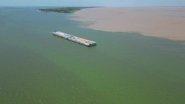 Aerial drone view of a cargo barge transporting truck trailers near the confluence of the Tapajos and Amazon rivers.