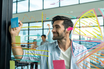 Portrait of young handsome businessman writing marketing idea by using colorful marker on glass...