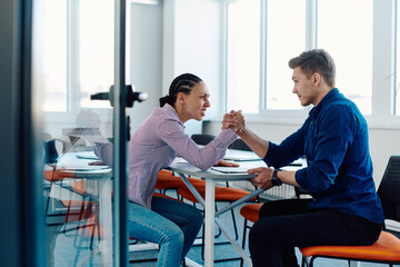 Obraz premium In a modern startup office, a businessman and a businesswoman business colleagues engage in a symbolic arm-wrestling match, reflecting teamwork, competition, and innovation in their dynamic workplace.