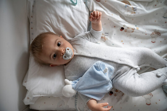 Baby lying on cozy bed with silicone soother in mouth