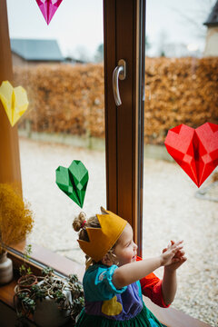 Birthday girl by the window. Kite paper hearts for decoration.
