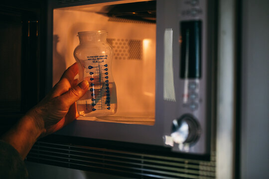 Woman taking baby bottle with water from microwave 