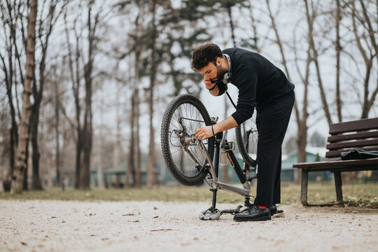 A professional businessman in casual attire taking a break to fix his bicycle in a serene park environment.