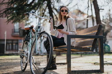 A fashionable woman listens to music with headphones while reading a book on a sunny day in the...