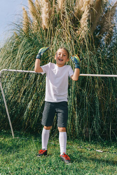 A girl in a sports uniform cheers at the soccer goal