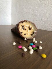 Ice cream cone filled with dulce de leche, chocolate, brigadeiro, coconut on wooden background with copy space
​