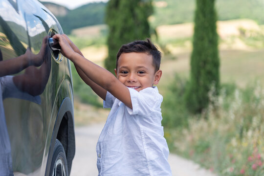 Cute boy about to open the car door and enjoys the landscape