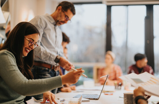 Enthusiastic colleagues engaging in teamwork and discussion over charts in a lively office setting, highlighting collaboration and a productive work atmosphere.