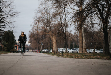 An active young woman enjoys a peaceful bike ride along a tree-lined path in an urban park, embodying leisure and a healthy lifestyle against an autumnal backdrop.