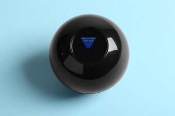 Magic eight ball with prediction Indications Say Yes on light blue background, above view