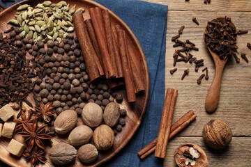 Spoon with different spices and nuts on wooden table, flat lay