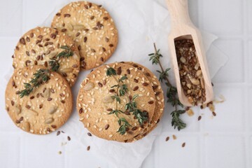 Cereal crackers with flax, sesame seeds, thyme and scoop on white tiled table, top view