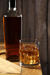 Whiskey with ice cubes in glass and bottle on wooden crate, closeup