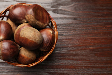 Sweet fresh edible chestnuts in wicker bowl on wooden table, top view. Space for text