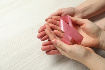 Breast cancer awareness. Women holding pink ribbon at white wooden table, closeup. Space for text