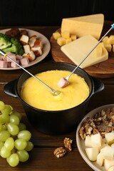 Fondue pot with melted cheese, forks and different products on wooden table
