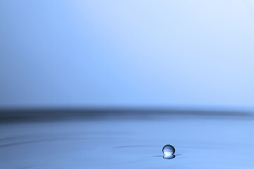 Drop falling into clear water on light grey background, closeup