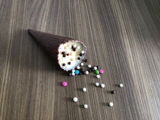 Ice cream cone filled with dulce de leche, chocolate, brigadeiro, coconut on wooden background with copy space
​