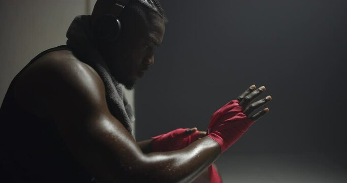 Black man, hands and boxer getting ready for competition or training at night, club or gym in locker room. African male person, athlete or fighter gloves in preparation for fight, MMA or self defense