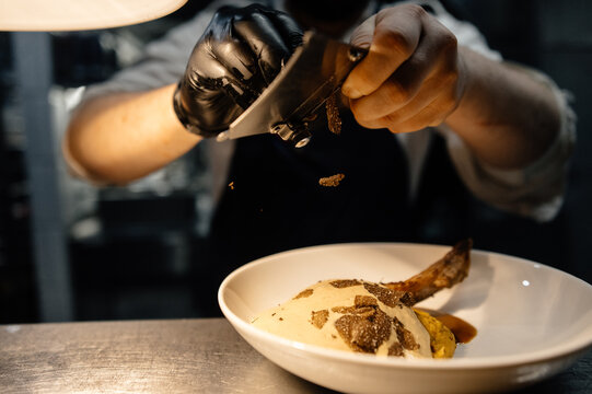 Crop chef grating truffle on steak standing at counter
