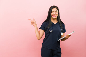 Excited medical nurse with scrubs smiling pointing to pink copy space ad