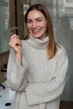 Smiling blonde girl holding aligner bracer in hand