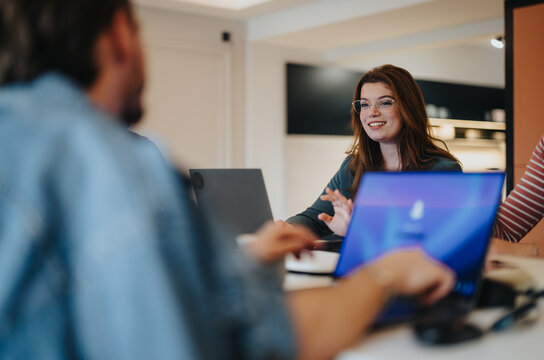Happy female person wearing glasses actively participating in a business team meeting. Office and teamwork concept captured in a modern workplace setting.
