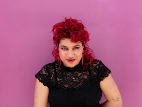 Non-binary person over pink background smiling at camera