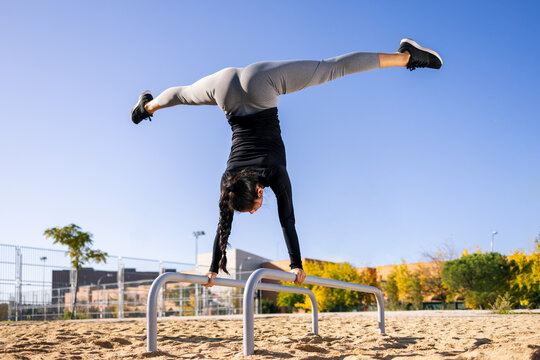 Confident sportswoman doing handstand with splits on parallel bars