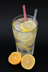 Refreshing lemonade in a tall faceted glass with ice and lemon slices on a black background.