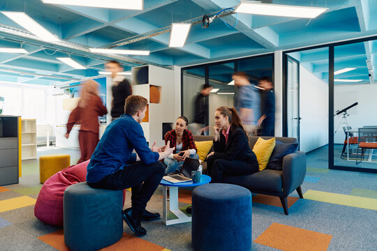 Multiethnic startup business team on meeting in a modern bright open space coworking office. Brainstorming, working on laptop. Group of coworkers walking around in motion blur
